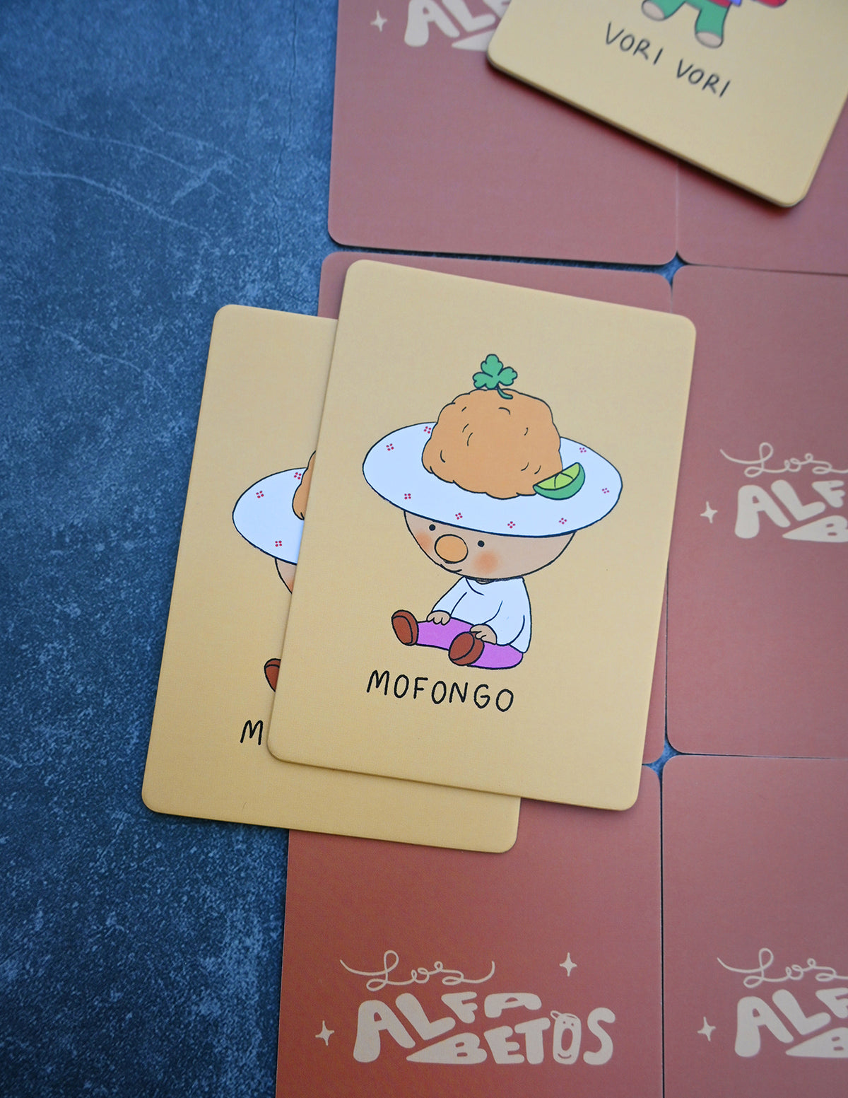 "Los Alfabetos" is a memory card matching game set of 26 pairs of Latin food characters. Designed by illustrator Natalí Koromoto Martínez.