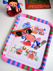Colorful tray with cartoon designs, sunglasses, and a watch on a white surface. Design by Natali Koromoto.