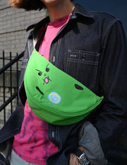 "Bad-nana" Crescent Bag. Natali Koromoto design NYC.
- A colorful cartoon illustration of a green banana-like character with an angry face and the words 'Lil' BAD NANA' on a solid pink background.